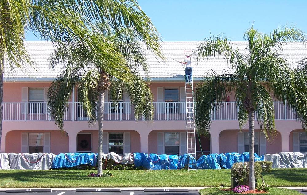 Two-storey condominium being cleaned from a ladder, with the planting beds tarped off below