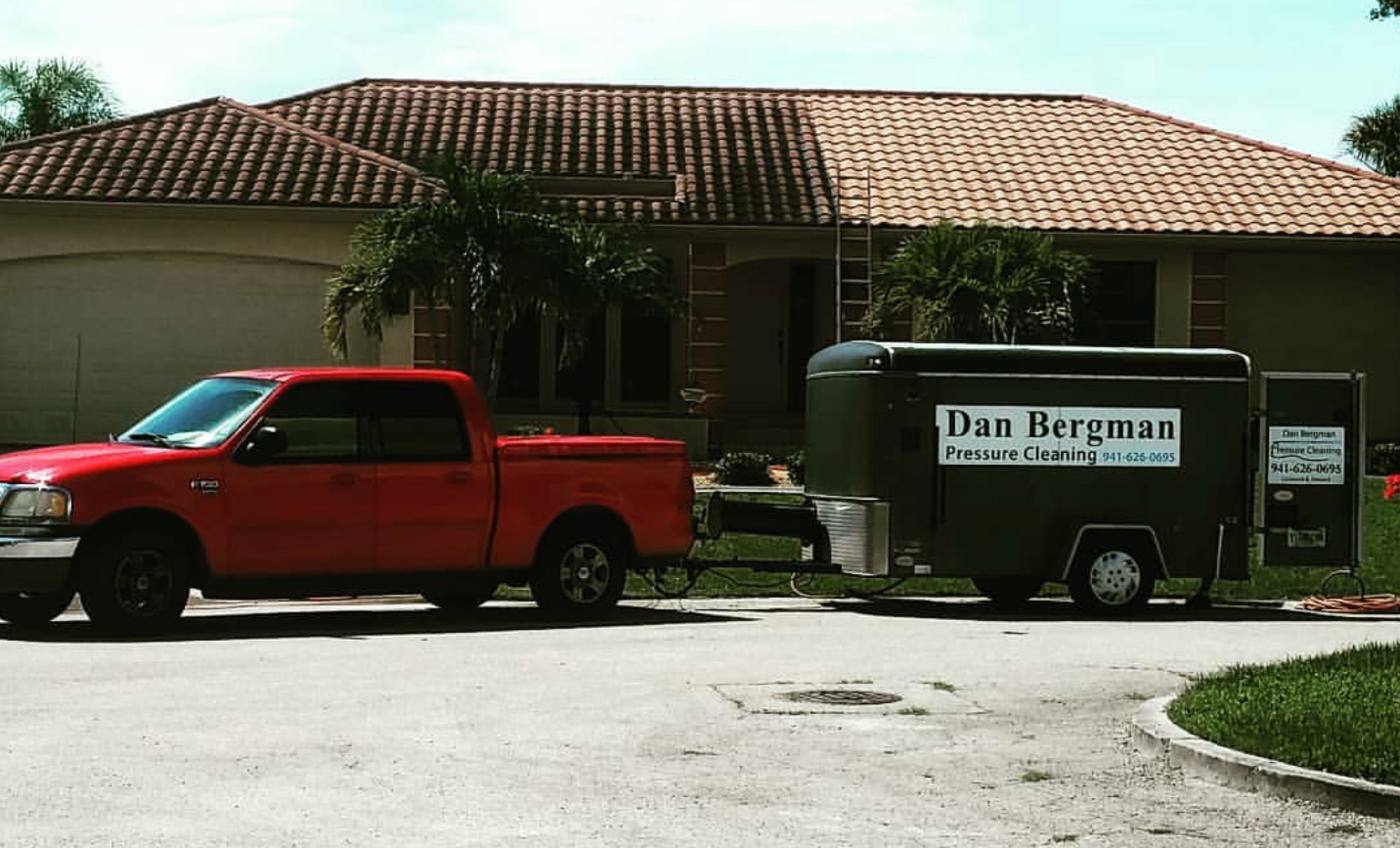 Red work truck and branded trailer outside a home with a cleaned terracotta tile roof